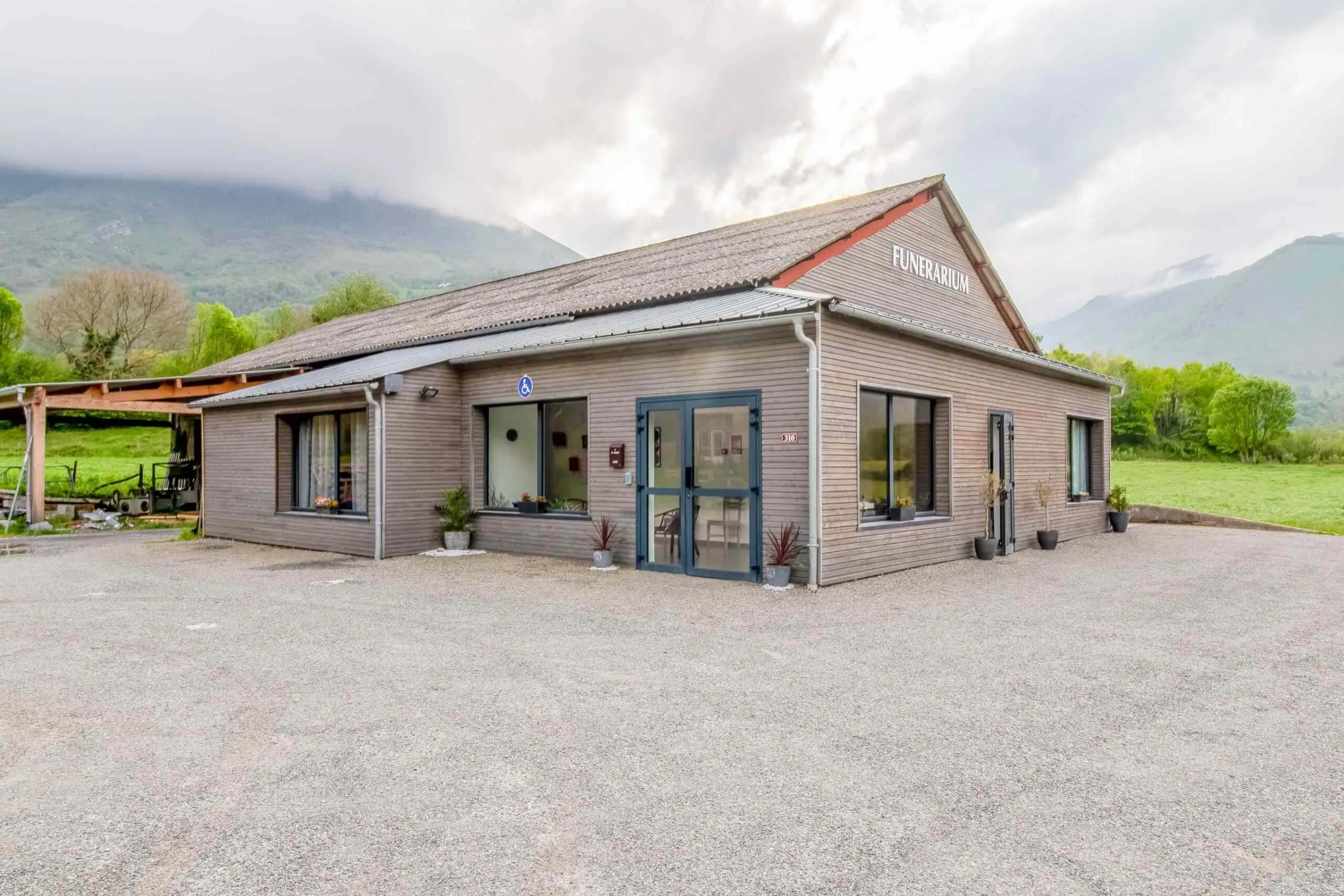 Façade en bois du funérarium et parking visiteurs avec vue sur la montagne